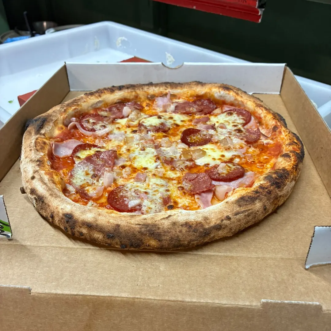 A wood-fired pizza with ham, salami and melted mozzarella in a Tano’s takeaway box